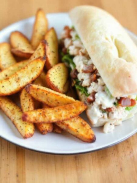 Plate of crispy air fryer potato wedges with spices, served alongside a chopped chicken caesar salad sandwich in a toasted sub roll.