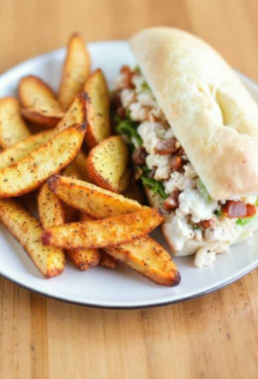 Plate of crispy air fryer potato wedges with spices, served alongside a chopped chicken caesar salad sandwich in a toasted sub roll.