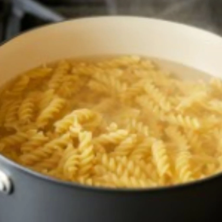 Close-up of egg noodles boiling in a pot with steam rising, showcasing the cooking process.