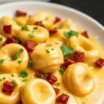 Close-up of creamy cheese marry me chicken tortellini garnished with fresh parsley and diced bacon, served on a white plate for a comforting meal.