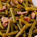 Cooked green beans mixed with tender bacon pieces served in a white bowl, showcasing a hearty and flavorful dish.