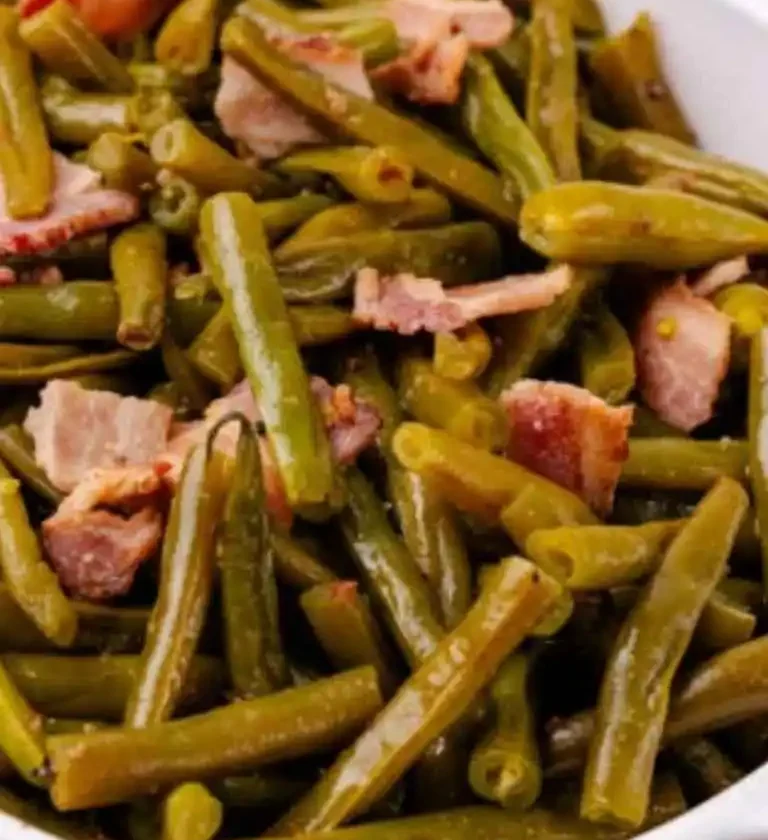 Cooked green beans mixed with tender bacon pieces served in a white bowl, showcasing a hearty and flavorful dish.