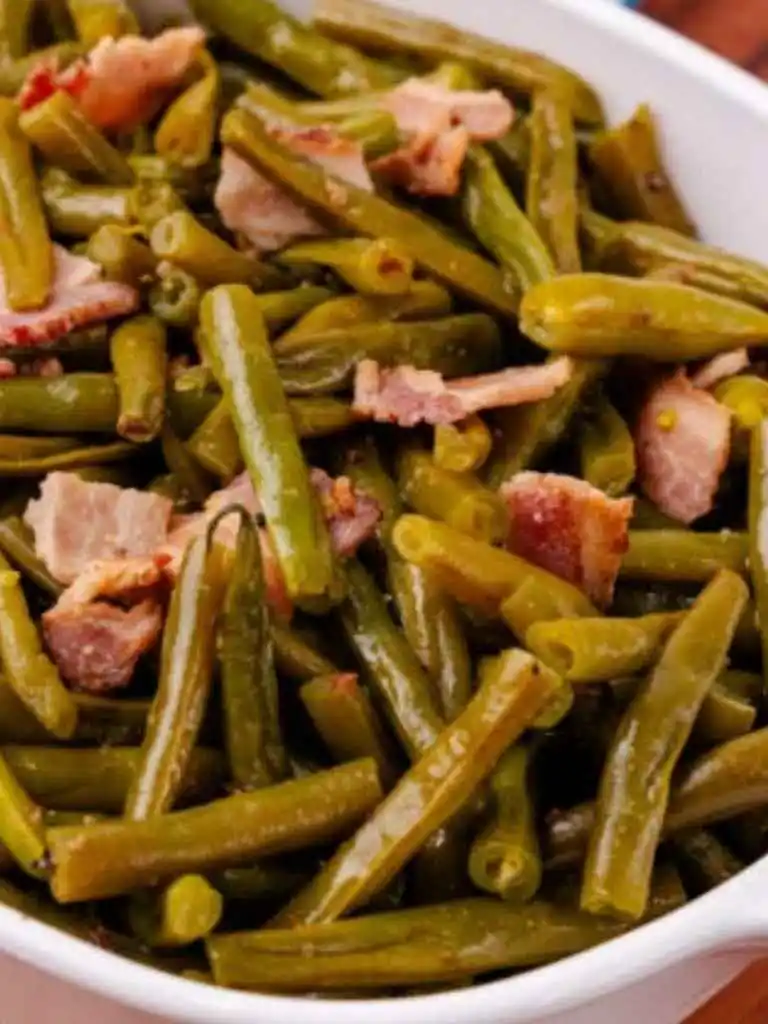 Cooked green beans mixed with tender bacon pieces served in a white bowl, showcasing a hearty and flavorful dish.