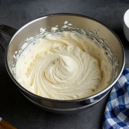 A smooth, creamy frosting swirled in a metal mixing bowl.