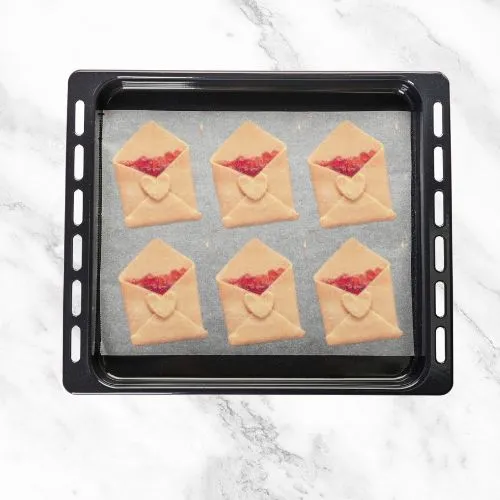 Baking tray with jam-filled dough parcels shaped like envelopes.