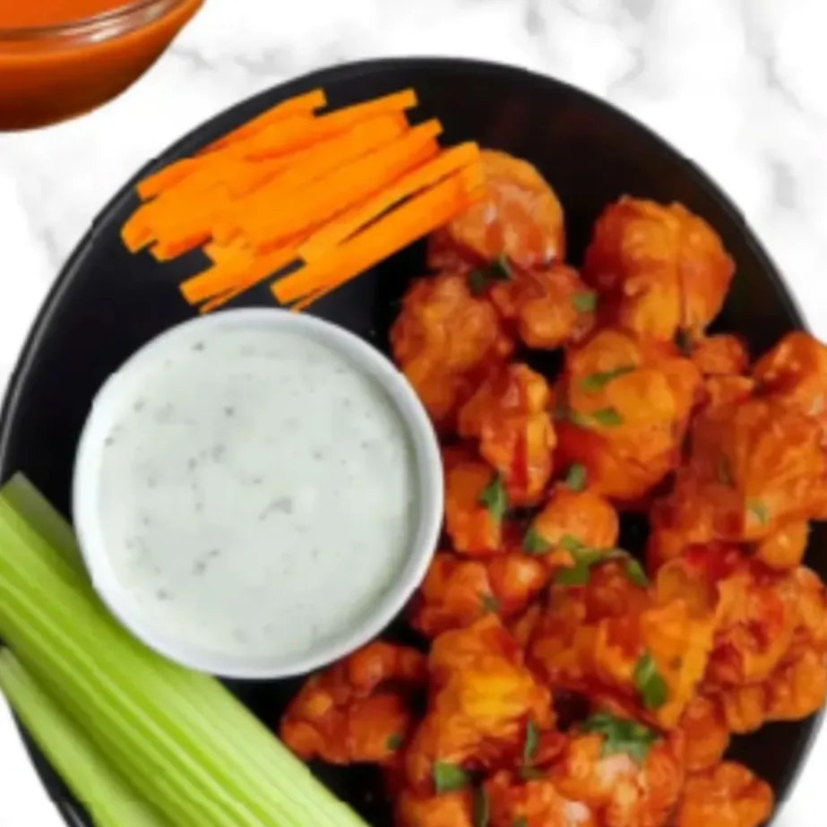 Air fryer buffalo cauliflower wings served with ranch dip, celery sticks, carrot sticks, and extra buffalo sauce in a black bowl.