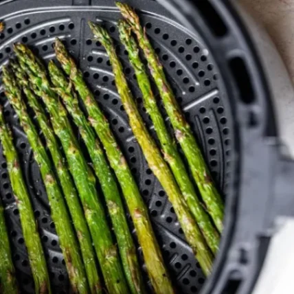 Fresh green asparagus spears roasted to perfection in an air fryer basket, lightly crisped and golden at the tips.