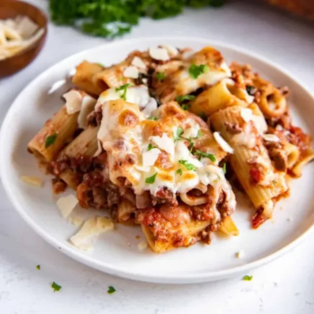 A serving of cheesy baked rigatoni with meat sauce, melted mozzarella, and fresh parsley on a white plate.