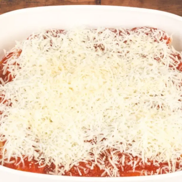 Unbaked cheesy baked rigatoni topped with a generous layer of shredded mozzarella cheese in a white baking dish.